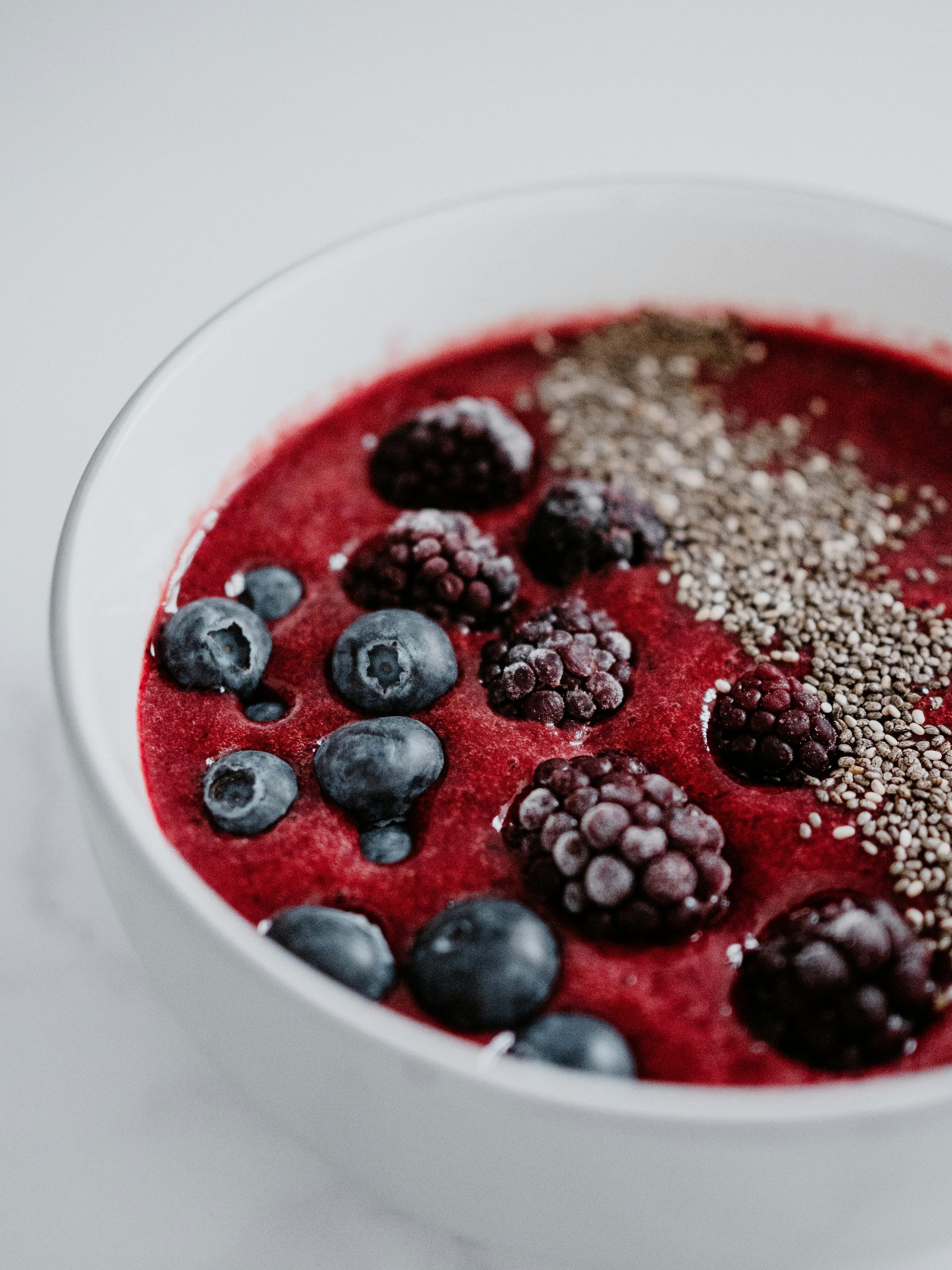 Egészséges reggeli: Krémes, sötétvörös színű smoothie bowl fehér tálban, friss (vagy fagyasztott) áfonyával, szederrel és chia mag szórással.